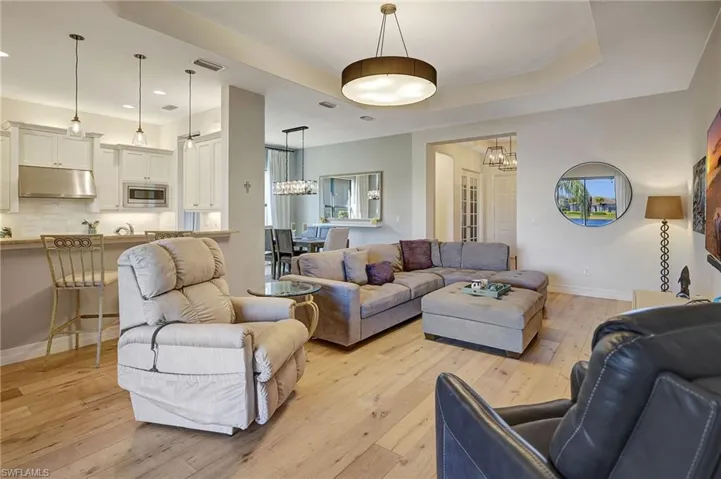 Living area with recessed lighting, a notable chandelier, baseboards, light wood-type flooring, and a tray ceiling