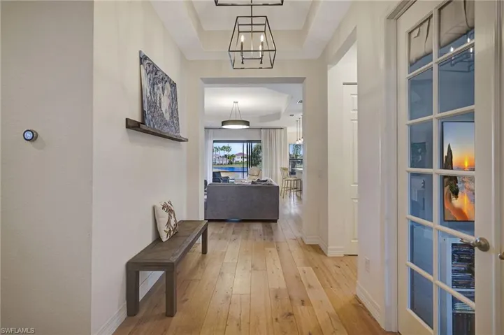 Hallway with light wood-type flooring, a raised ceiling, baseboards, and an inviting chandelier