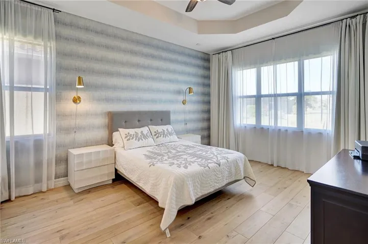 Bedroom featuring light wood finished floors, ceiling fan, and a tray ceiling