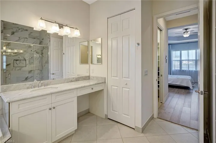 Ensuite bathroom featuring a ceiling fan, baseboards, vanity, a marble finish shower, and tile patterned floors