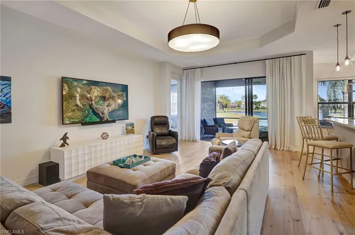 Living area featuring light wood-style floors, a raised ceiling, visible vents, and baseboards