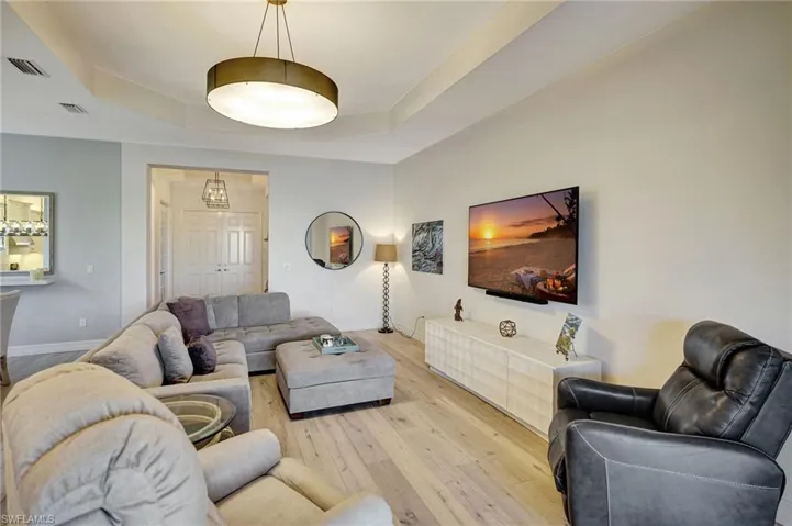 Living room featuring light wood finished floors, a tray ceiling, visible vents, and baseboards