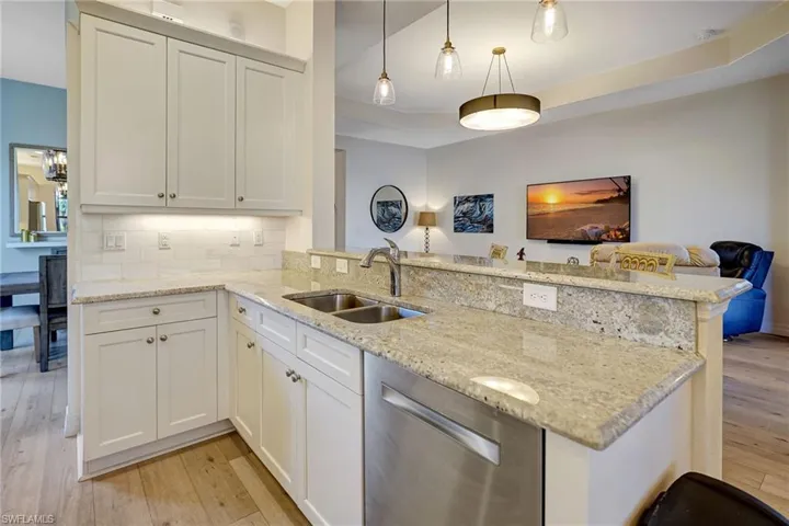 Kitchen with a peninsula, stainless steel dishwasher, a sink, and light wood-style flooring