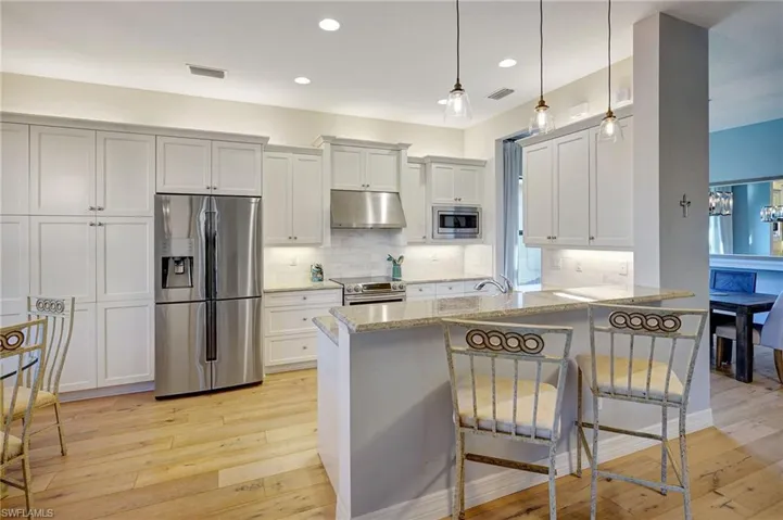 Kitchen featuring visible vents, appliances with stainless steel finishes, light wood-type flooring, under cabinet range hood, and a kitchen bar