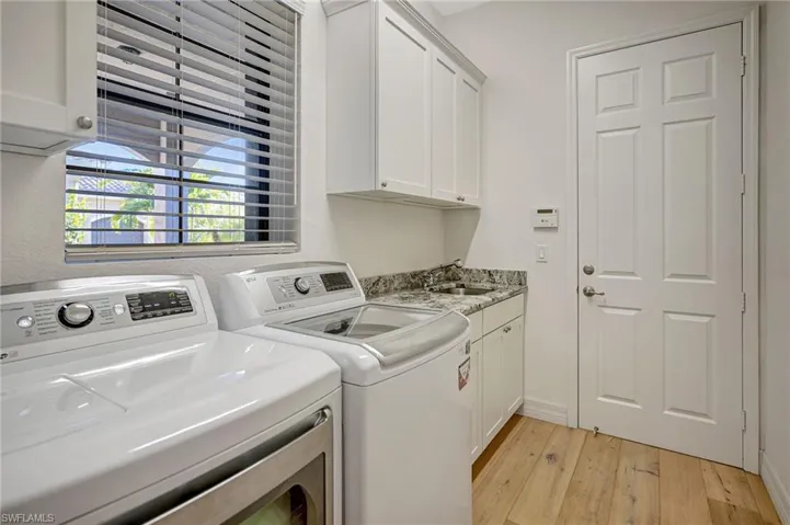 Clothes washing area featuring cabinet space, a sink, light wood-style flooring, and washing machine and clothes dryer