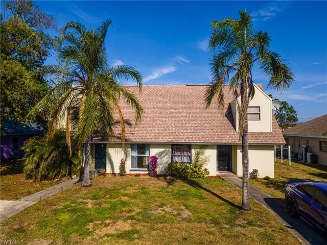 View of front of property with a shingled roof, a front yard, and stucco siding