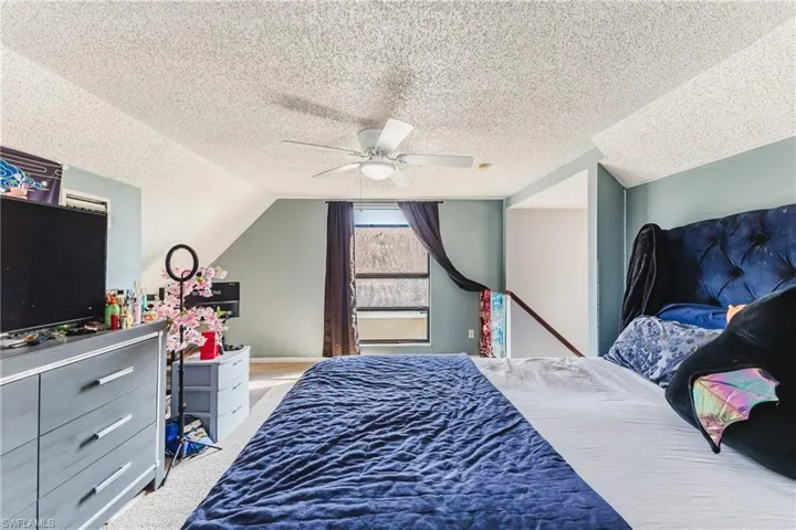 Carpeted bedroom with vaulted ceiling, ceiling fan, and a textured ceiling