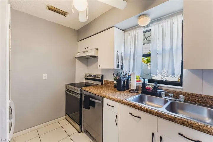 Kitchen with stainless steel appliances, white cabinetry, dark countertops, a textured ceiling, and under cabinet range hood