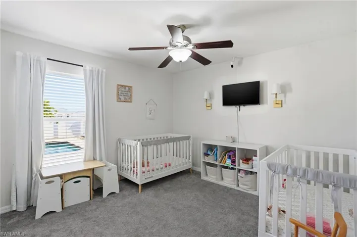 Bedroom featuring a nursery area, carpet flooring, and a ceiling fan