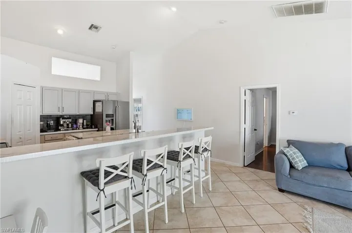 Kitchen featuring a kitchen bar, high vaulted ceiling, high end refrigerator, light tile patterned floors, and gray cabinetry