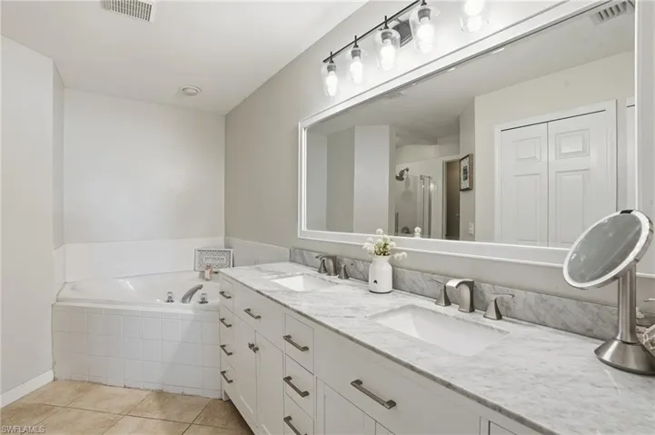 Bathroom featuring a garden tub, a shower stall, double vanity, and light tile patterned floors