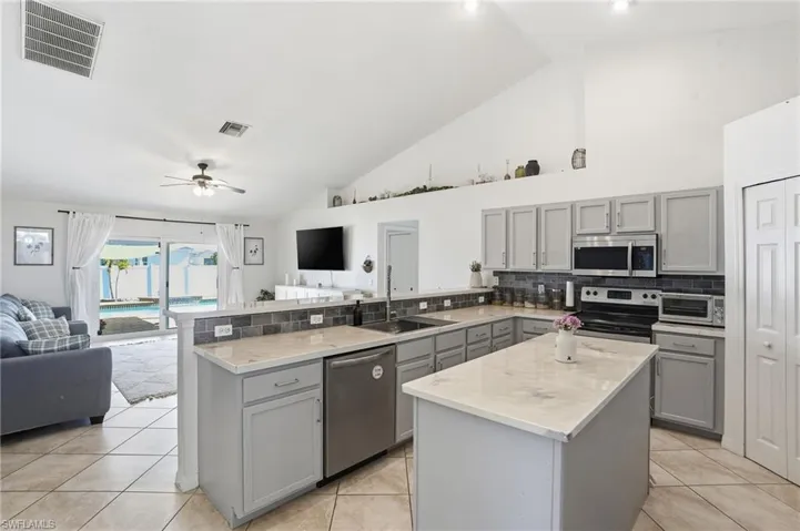 Kitchen with gray cabinets, open floor plan, a center island, appliances with stainless steel finishes, and high vaulted ceiling