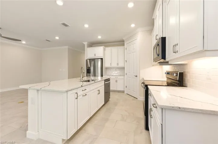 Kitchen featuring stainless steel appliances, light stone countertops, white cabinetry, crown molding, and a kitchen island with sink