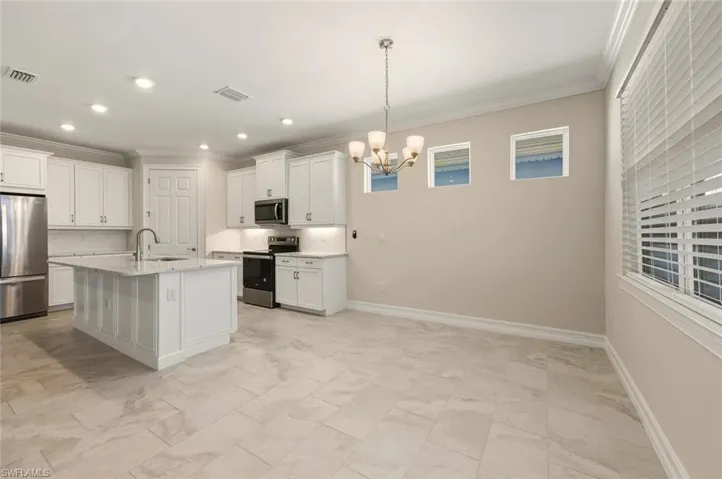 Kitchen with stainless steel appliances, white cabinetry, decorative backsplash, ornamental molding, and a chandelier