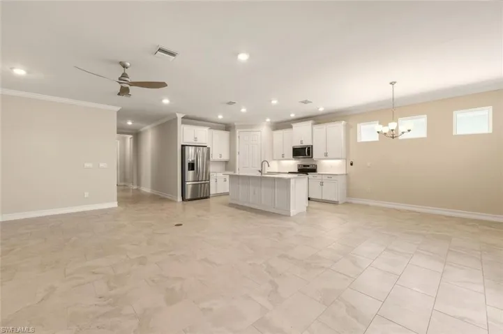 Kitchen with open floor plan, light countertops, white cabinets, stainless steel appliances, and ornamental molding