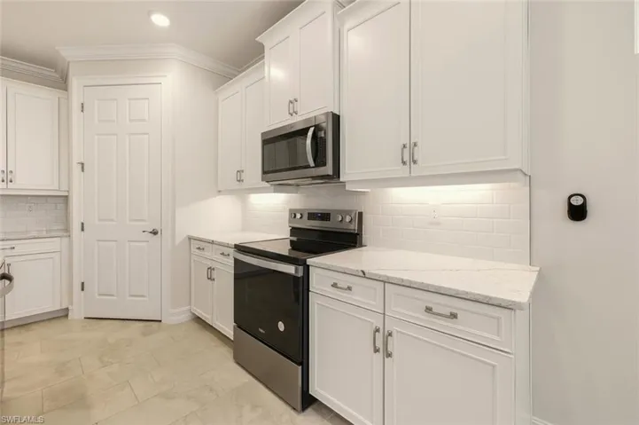 Kitchen with stainless steel appliances, white cabinets, ornamental molding, decorative backsplash, and light stone counters