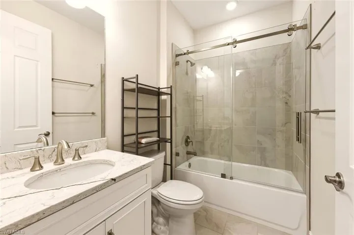 Bathroom featuring vanity, bath / shower combo with glass door, and tile patterned flooring