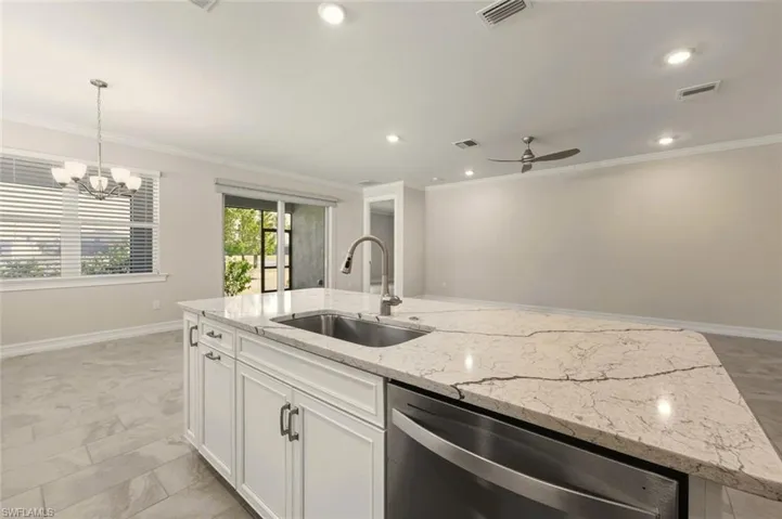 Kitchen with stainless steel dishwasher, white cabinets, light stone counters, a center island with sink, and a chandelier