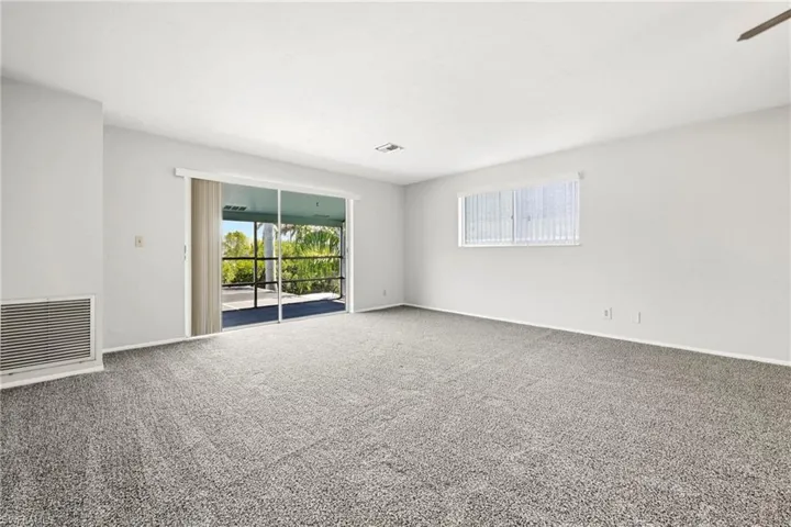 Spacious interior room featuring light gray carpeting, white walls, and a sliding glass door providing access to an outdoor screened area
