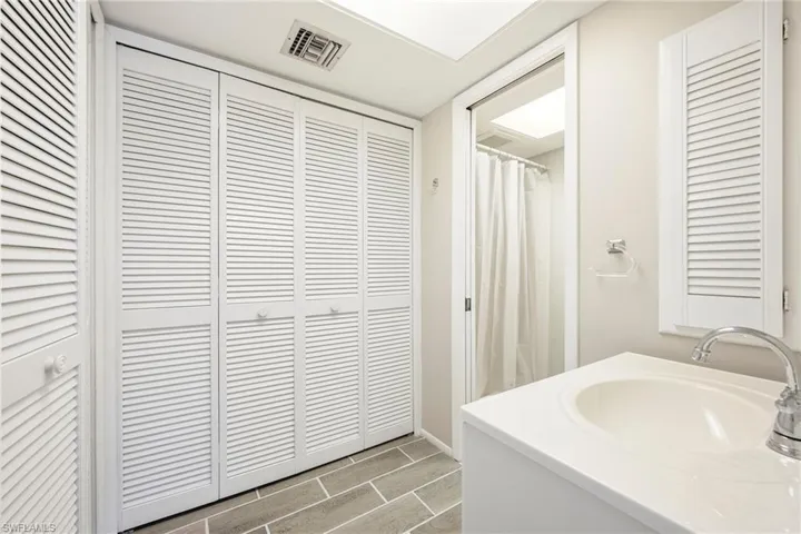 Bathroom featuring louvered bi-fold closet doors, a single vanity with an integrated sink, a chrome faucet, and gray wood-finish floor tiles