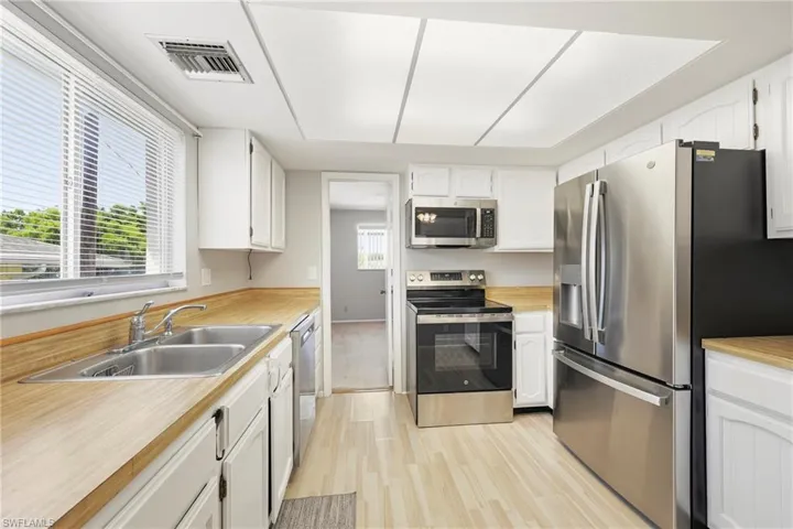 Kitchen featuring light wood-finish flooring, white cabinetry, wood-finish countertops, a stainless steel double-basin sink, and a suite of stainless steel appliances