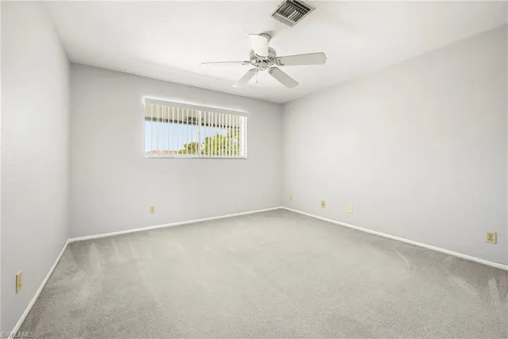 Spacious interior room featuring light gray carpeting, white walls, and a ceiling fan