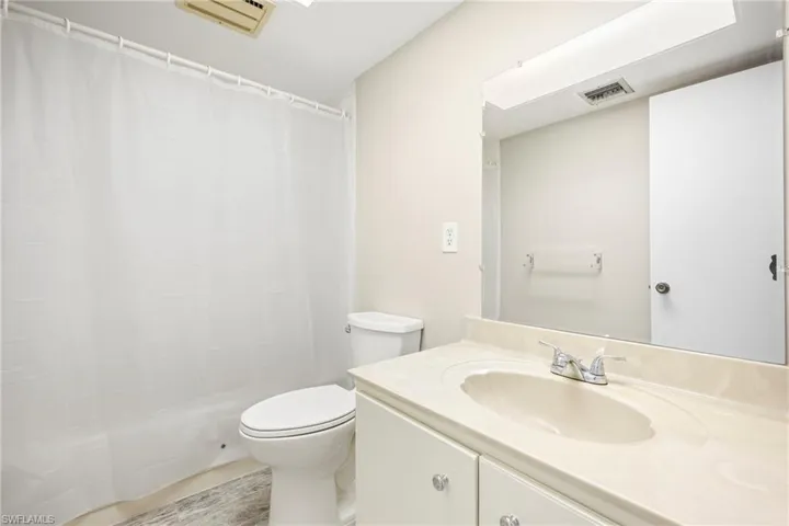 Bathroom featuring a light-colored vanity with an integrated sink, a large wall-mounted mirror, brushed chrome faucet, and a toilet