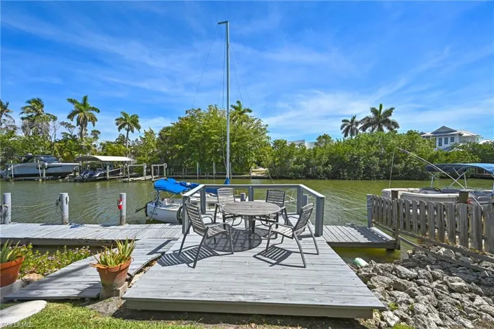 Waterfront property featuring a private dock with multiple slips, a spacious outdoor deck, mature palm trees, and lush tropical foliage