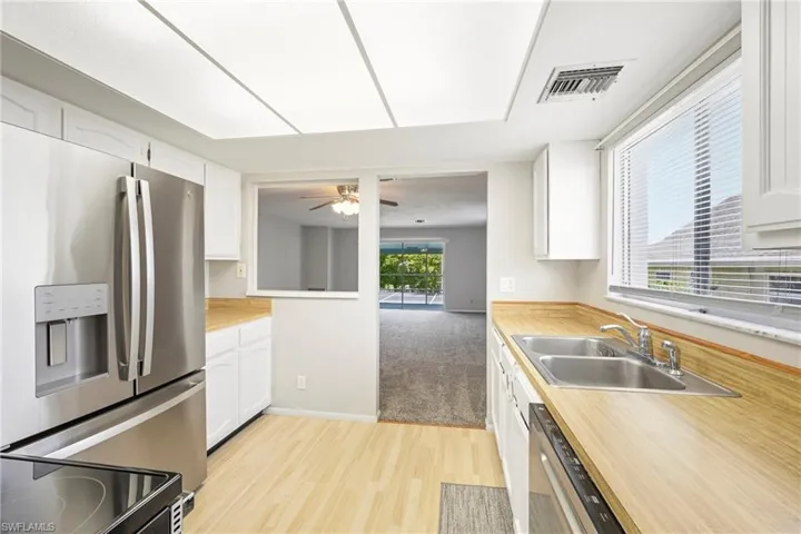 Kitchen featuring wood-finish flooring, white cabinetry, wood-finish countertops, stainless steel appliances, and a dual basin sink