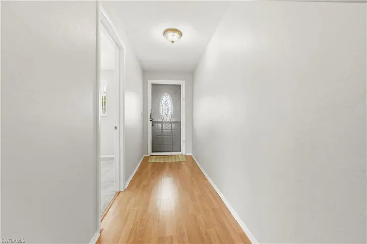 Inviting entry hallway featuring wood-finish flooring, light neutral wall tones, and a decorative glass-insert door