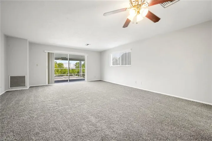 Spacious room featuring light gray carpeting, neutral wall finishes, and a ceiling fan with integrated lighting