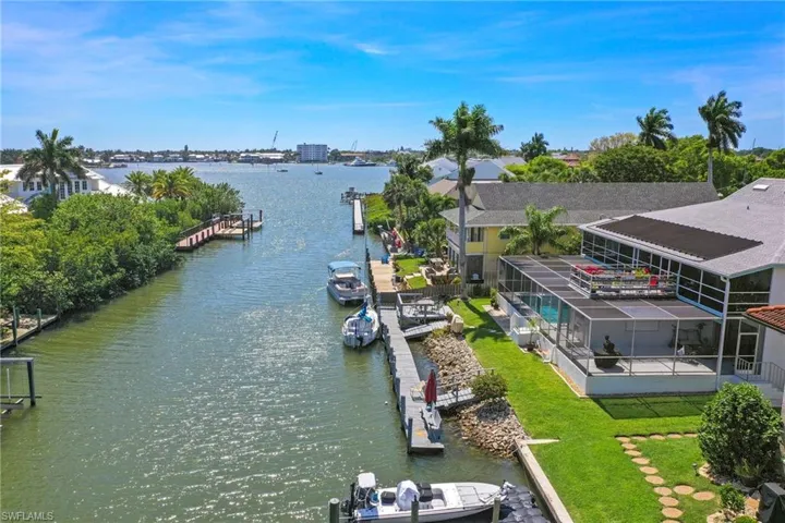 Waterfront canal property featuring a private boat dock, enclosed swimming pool, covered outdoor patio, and a manicured lawn