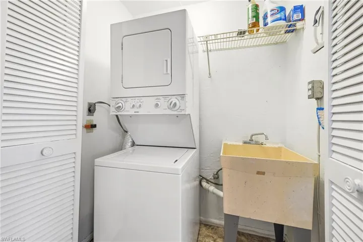 Dedicated laundry area featuring a stacked washer and dryer unit, utility sink, and overhead wire shelving