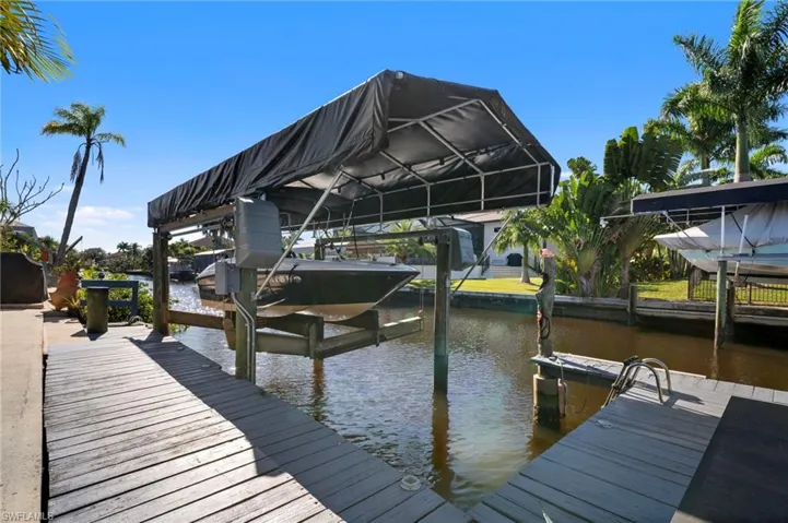 Waterfront canal access featuring a covered boat lift, extensive wooden decking, and mature palm trees
