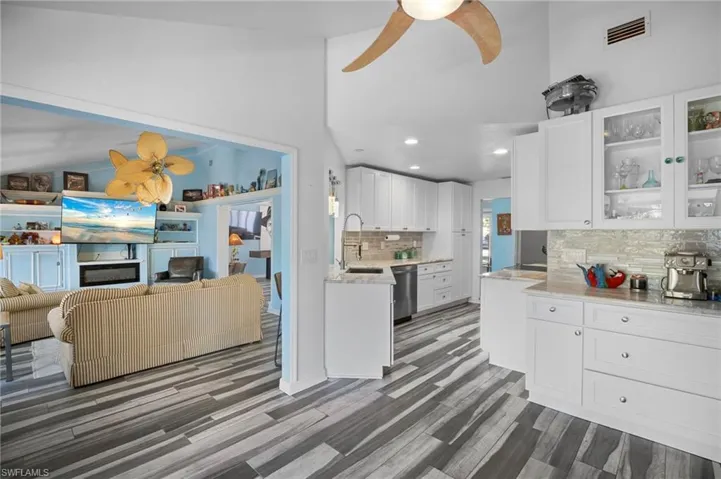 Kitchen and living area featuring wood-finish flooring, white cabinetry with glass-front uppers, stainless steel appliances, and a tile backsplash