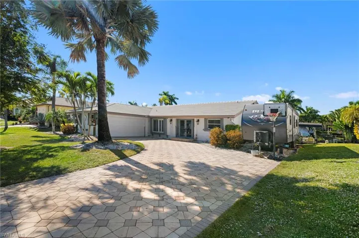 Exterior featuring a paver driveway, mature palm trees, a well-maintained lawn, multiple entry doors, and an attached garage