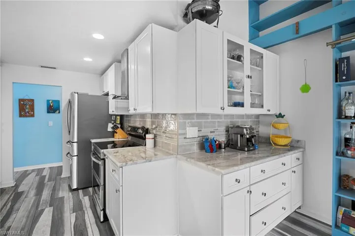 Modern kitchen featuring white cabinetry with glass-front accents, light-toned countertops, and a gray subway tile backsplash
