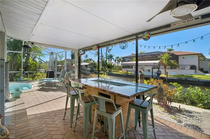 Screened outdoor living area featuring a built-in bar with a stone-finish countertop, herringbone brick paver flooring, and a ceiling fan