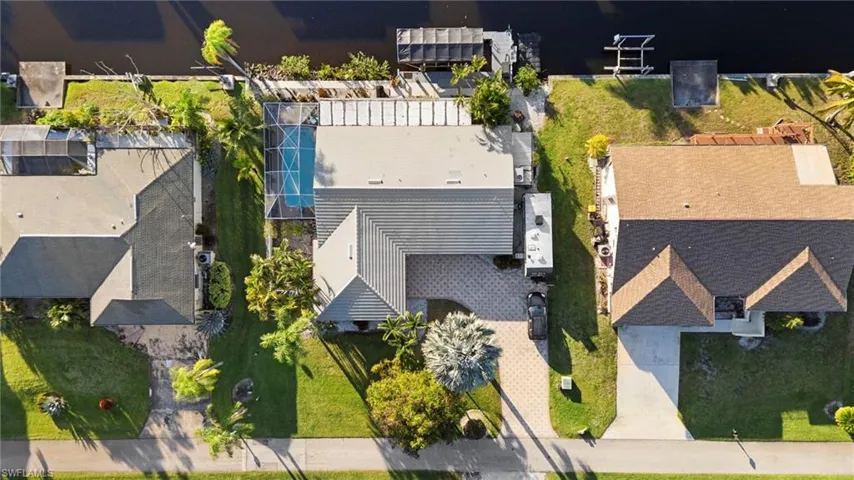 Canal-front property featuring a screened-in swimming pool and mature landscaping
