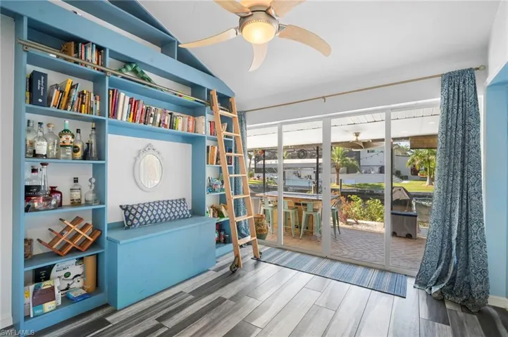 Built-in shelving unit with a rolling ladder, wood-finish flooring, sliding glass doors, and a ceiling fan