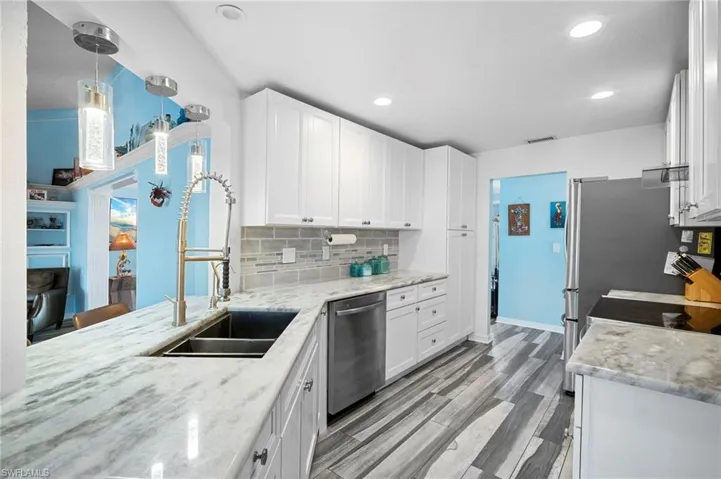 Kitchen featuring white cabinetry, light-toned stone countertops, and wood-finish flooring