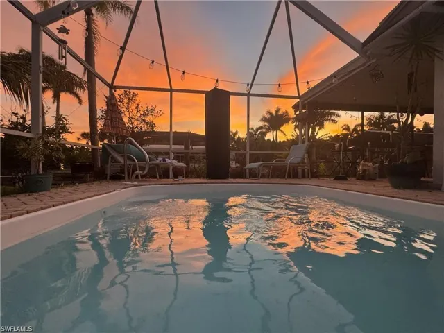 Screened-in pool area featuring a rectangular pool, brick paver decking, and a covered patio section