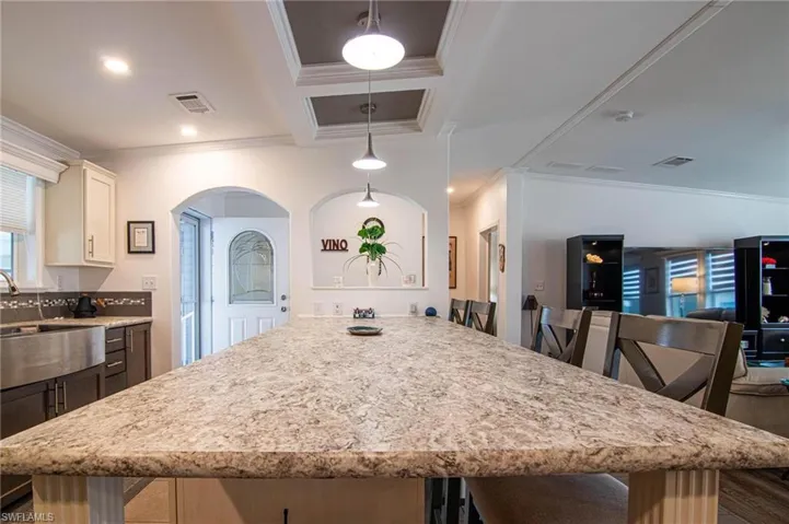 Kitchen featuring light stone countertops, crown molding, a kitchen bar, white cabinetry, and open floor plan