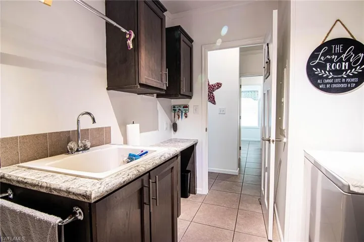 Kitchen featuring dark brown cabinetry, light tile patterned flooring, washer / clothes dryer, and crown molding
