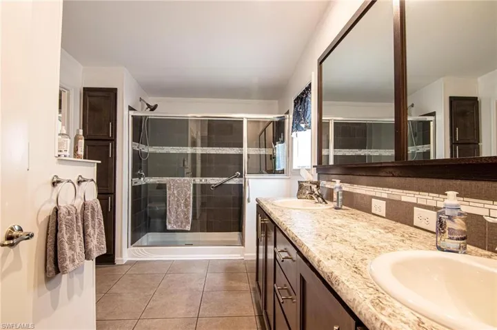 Full bathroom featuring double vanity, a shower stall, light tile patterned floors, and backsplash