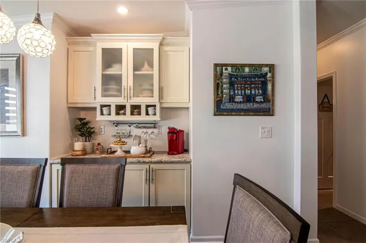 Bar area featuring ornamental molding, glass insert cabinets, pendant lighting, light stone countertops, and dark tile patterned flooring