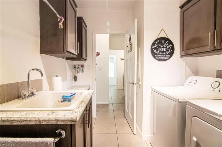 Washroom featuring cabinet space, light tile patterned floors, washer and dryer, and attic access