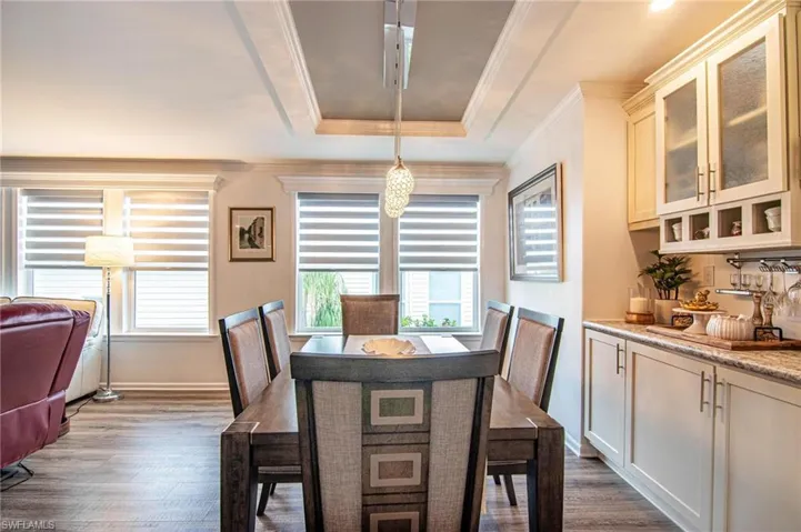 Dining space featuring a raised ceiling, dark wood-style flooring, and ornamental molding