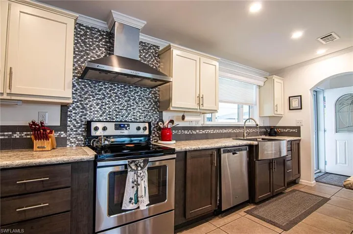 Kitchen featuring stainless steel appliances, backsplash, wall chimney range hood, light tile patterned flooring, and ornamental molding