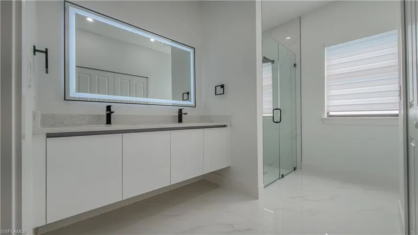Bathroom with a marble finish shower, light marble finish floors, and double vanity